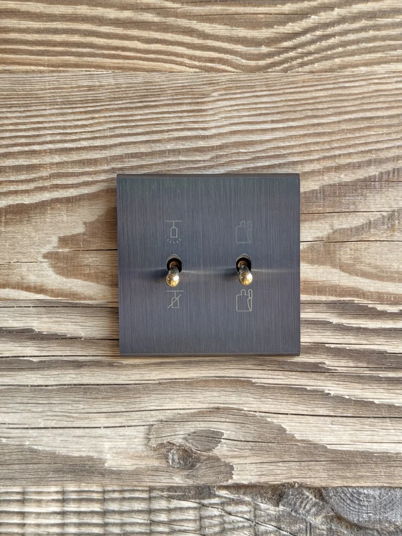 Plaque métallique à deux leviers, gravée de pictogrammes, sur un fond bois.