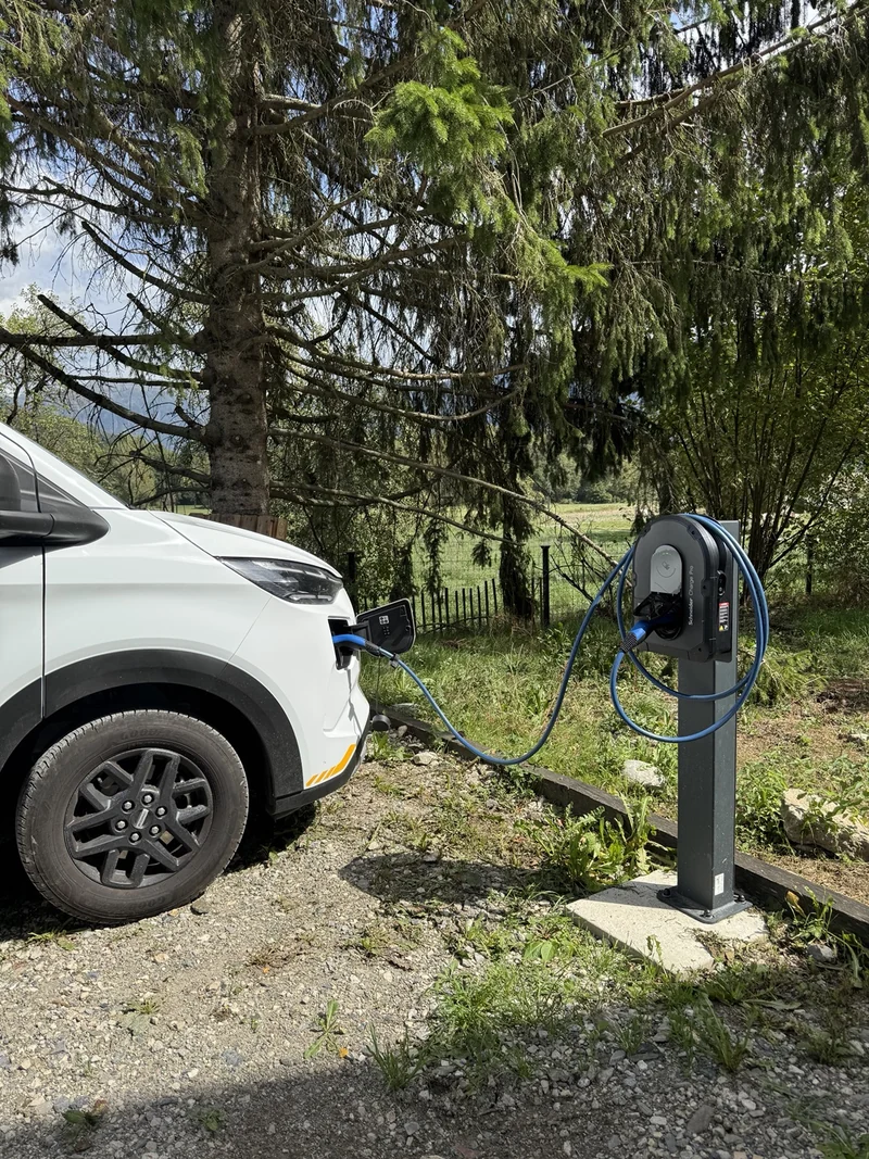 Véhicule électrique blanc branché à une borne Schneider sur pied, en extérieur.