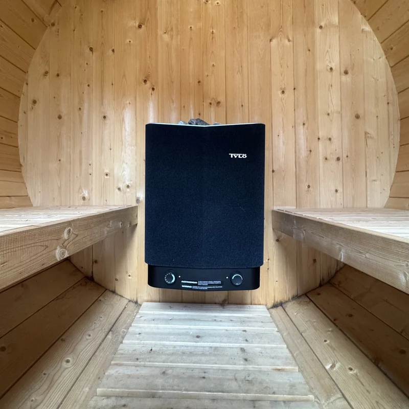 Poêle électrique de sauna noir installé entre deux banquettes en bois.